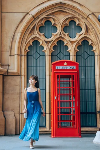 一位穿着蓝色连衣裙的女士走过一个红色的电话亭。