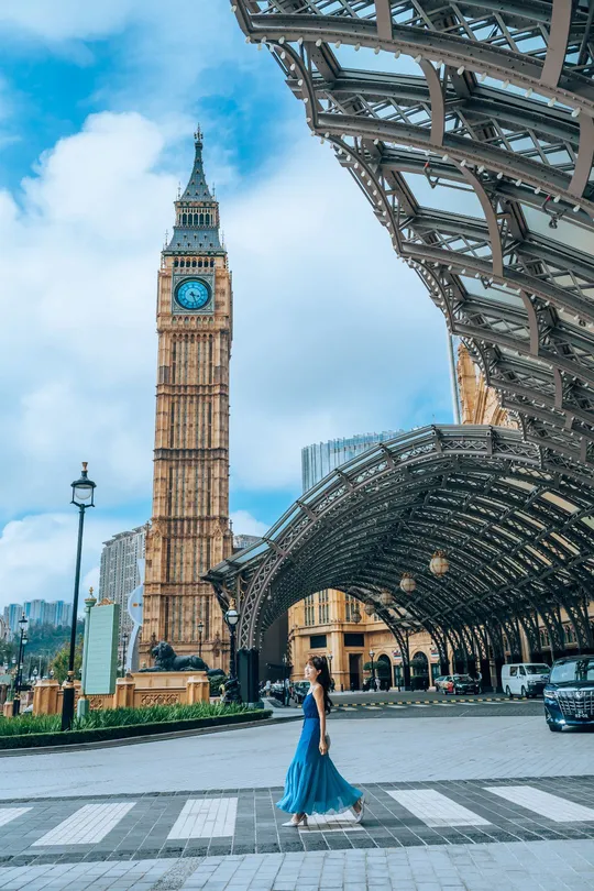 一位穿着蓝色连衣裙的女人站在城市的一座钟楼下面