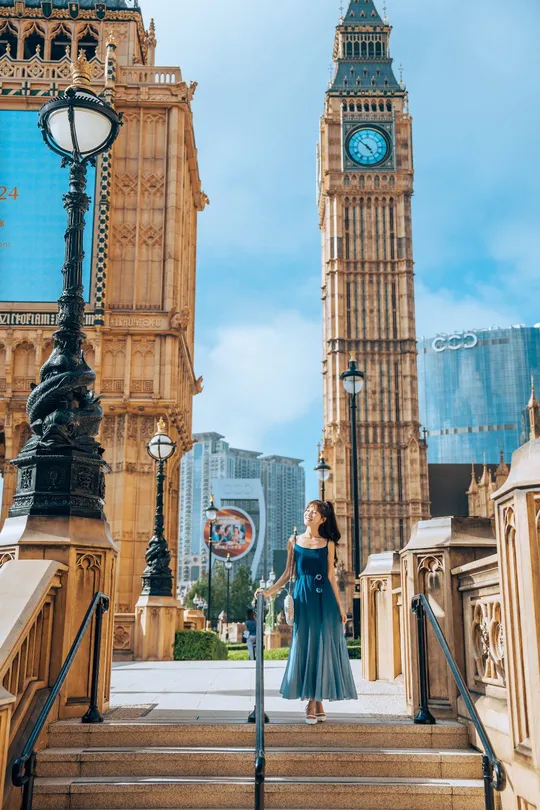 一位穿着蓝色连衣裙的女人站在一座有钟楼作背景的建筑的台阶上