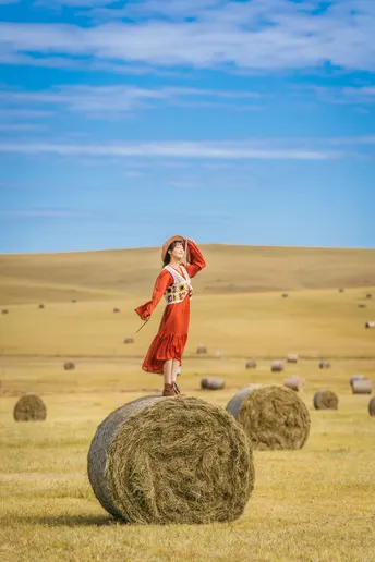 一个穿着红裙子的年轻女子站在一捆干草上。