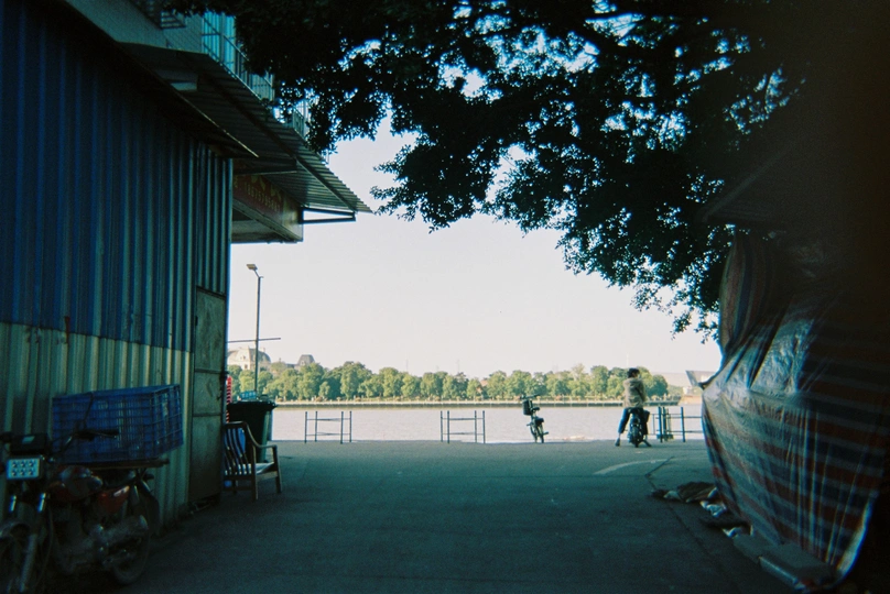 一个人在滑板上 一个人在摩托车上 摩托车停在靠近船只的水边建筑物旁边。