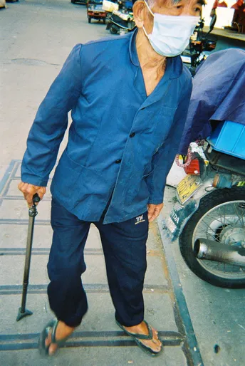 一个戴蓝色面罩的老先生推着助行器在人行道上行走。