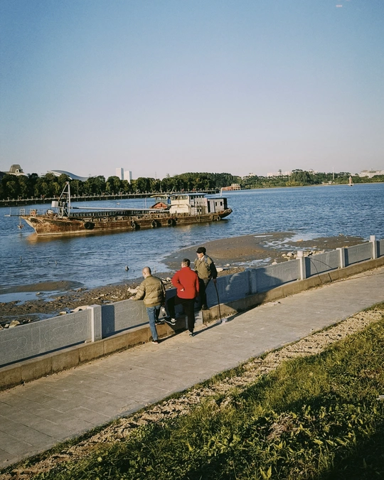 一些人在人行道旁边的水体旁的一张长椅上坐着。