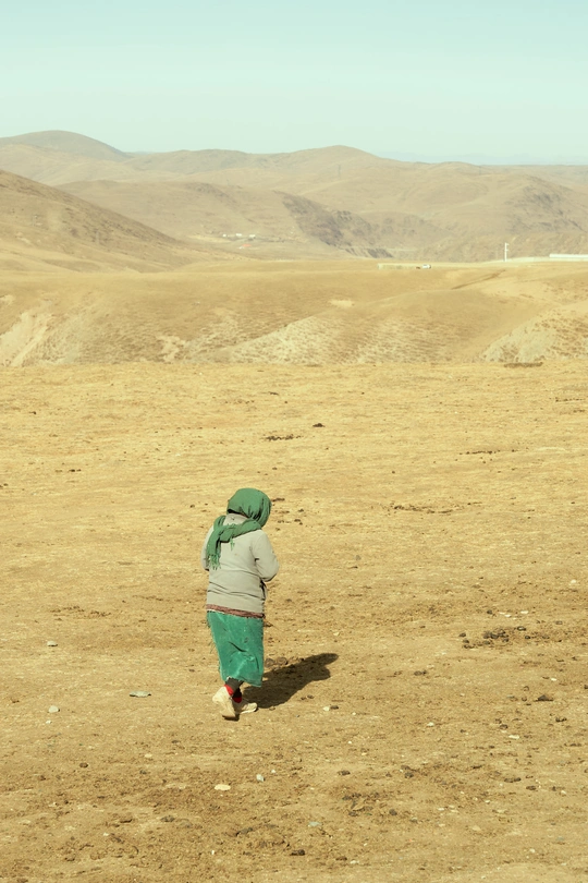 一位穿着绿色衣服的女人穿越沙漠 远处有山丘和山脉。