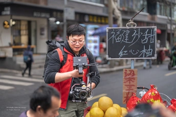 一位站在街上的男子 带着相机在给一个水果摊拍照。