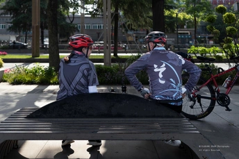 一对带着头盔的人坐在长凳上 而一名骑自行车的人正在骑车。