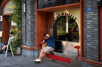 一个商店前 一个人坐在人行道上的长椅上 从窗口看到街上的人们正在走动。