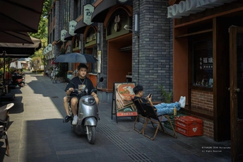 一个男子骑着滑板车沿着街道带着一个女子骑摩托车和一个拿伞的人。