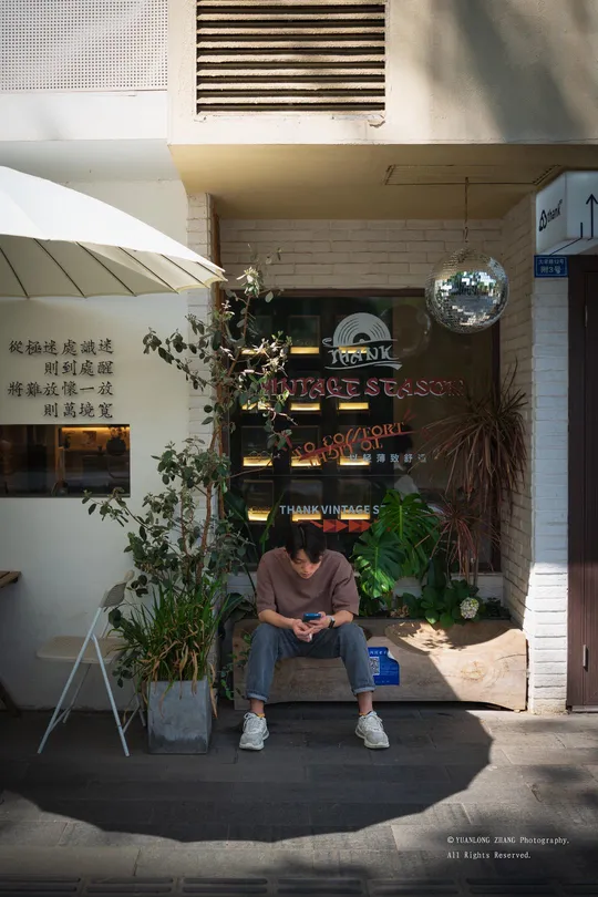 一位坐在商店前的长椅上 在遮阳伞下的男人。