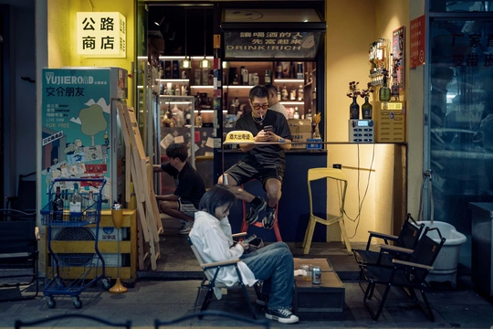 一个坐在理发店门口椅子上的男子 同时有一个人在给一个男子理发。
