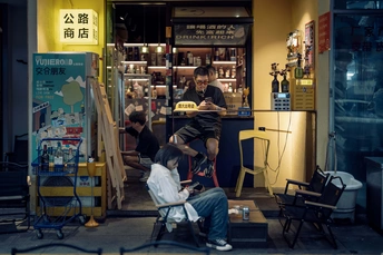一个坐在理发店门口椅子上的男子 同时有一个人在给一个男子理发。