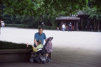 一个抱着婴儿坐在婴儿车上的女人和一个推着坐在长凳上的小孩的男人。