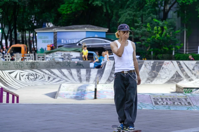 一个年轻人在滑板公园骑滑板 一个女子站在他身后。