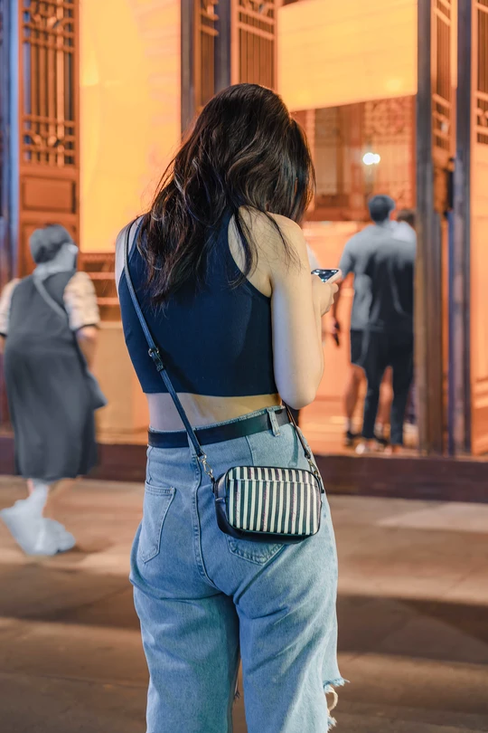 一位穿着蓝色牛仔裤的年轻女子在晚上走街时看着手机