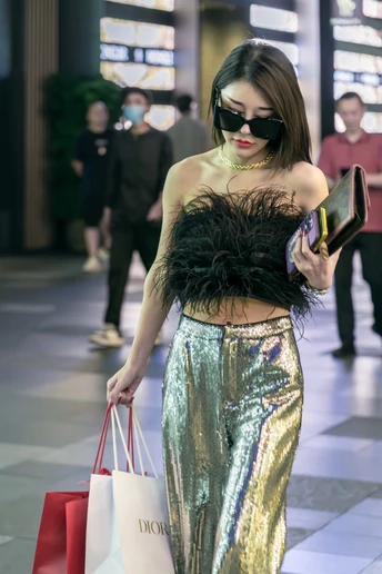 一个穿着闪亮金属服装的女人拿着购物袋在商场里走