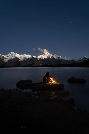 一个人坐在湖边岩石上 夜晚 远处有积雪的山峰。