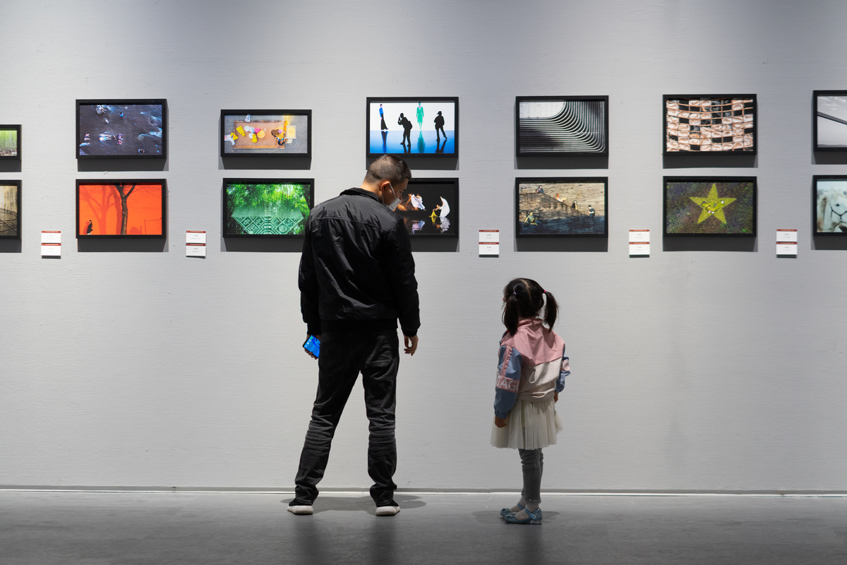 一个男子和女子带着一个小女孩站在艺术画廊里 注视着墙上的画。