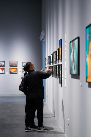 一个男子站在艺术画廊里 正在看墙上挂着的艺术作品图片。