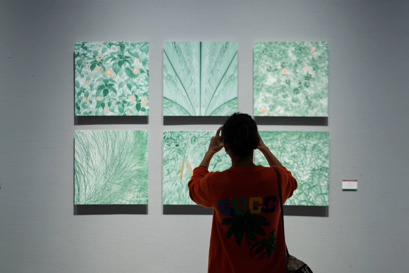 一个穿橙色衬衫的男子站在一个有画作的房间里 一个女子正在窗户旁