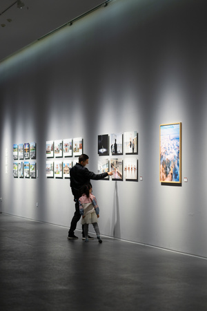 一个带着孩子的男人和女人正在穿过一个艺术画廊 看着墙上的画。