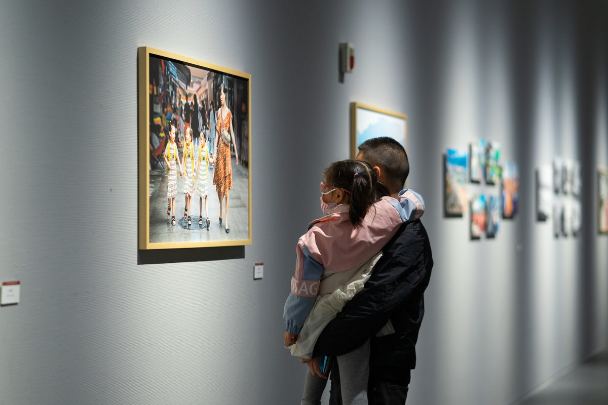 一个男子拥抱着一个站在艺术画廊里的年轻女孩 她正在看墙上的画；一个女子拥抱着一个年轻的孩子。
