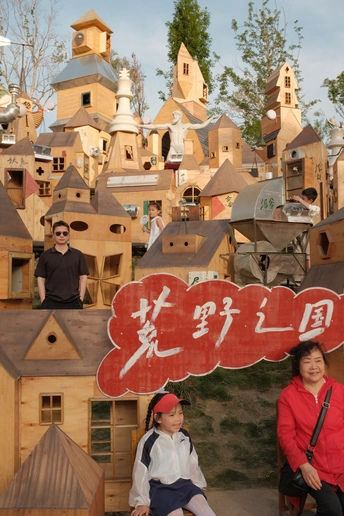 一位妇女和儿童在木质建筑群前为一张照片摆姿势 前面有一个写着hello的牌子 一群人在那里。