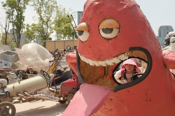 一座巨大的红色鸟类雕塑位于街道中央 周围停着车辆和摩托车。