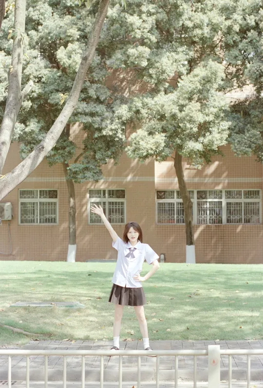 一个小女孩站在围栏前和树旁