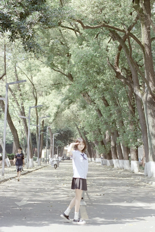 一位年轻女子站在公园里 周围有树木和一个小女孩。