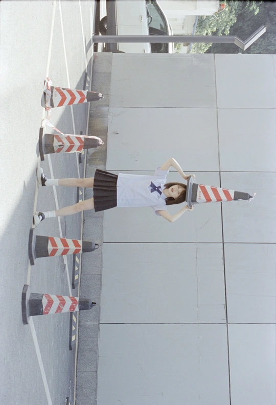 一位年轻女子站在梯子旁边 紧邻墙壁 手里拿着滑板。