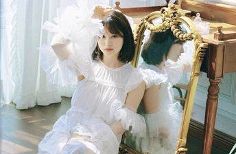 一位穿着白色连衣裙的年轻女子坐在镜子前的一把椅子上