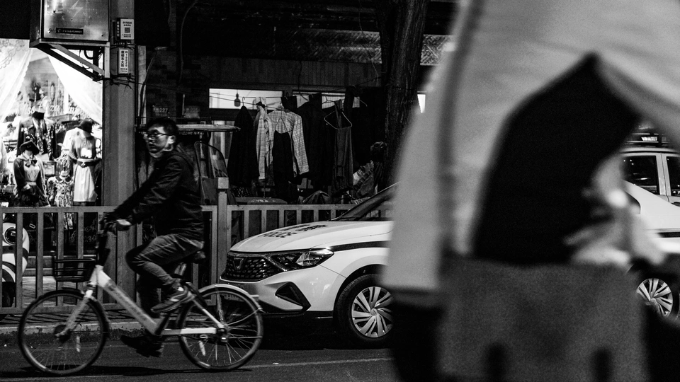 一张黑白照片 夜晚街道 有人行走 有人骑自行车。