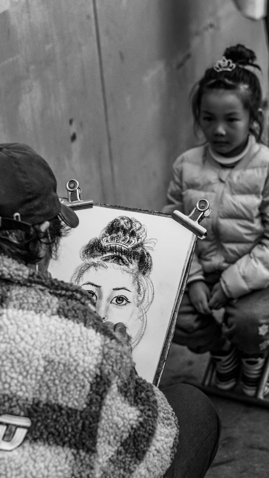 一张黑白照片 一个男子拿着一张画着女人坐在小女孩旁边的画。