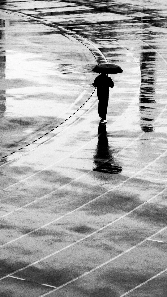 一个带着冲浪板和雨伞的男子走在湿漉漉的人行道上