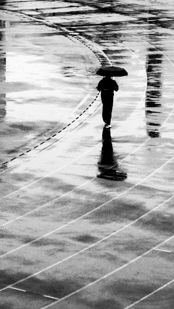 一个带着冲浪板和雨伞的男子走在湿漉漉的人行道上