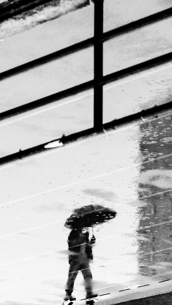 一张黑白照片 一个人在雨中撑着伞走。