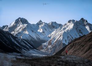 一个人站在白雪皑皑的山峰前 一架飞机从头顶飞过。