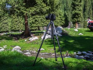 在一片田野中间 有一架放在三脚架上的相机 周围是岩石和树木。