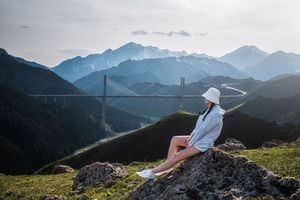 一位年轻女子坐在山顶的一块岩石上 俯瞰着一个山谷和一个桥。