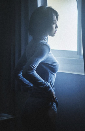 一个年轻的女人坐在黑暗的房间里 蓝色的灯光从窗户射进来