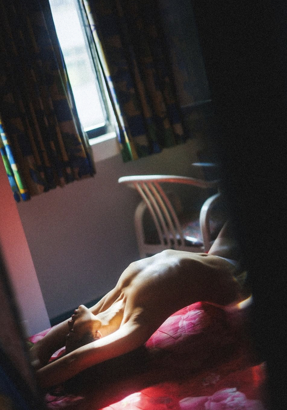 一个人躺在黑暗的房间里的床上 窗户边放着一台笔记本电脑 背景是一只正在睡觉的狗