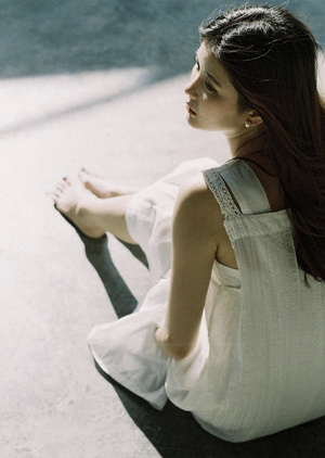一个穿着白色连衣裙的年轻女子坐在路缘上