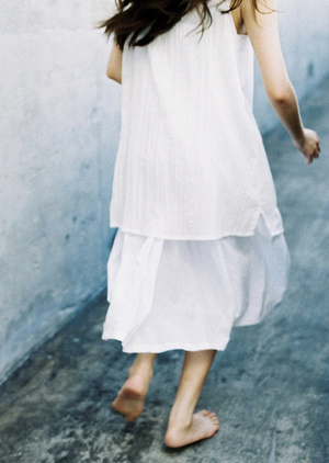 一位长发年轻女子穿着白色连衣裙在街上打着伞走下街道
