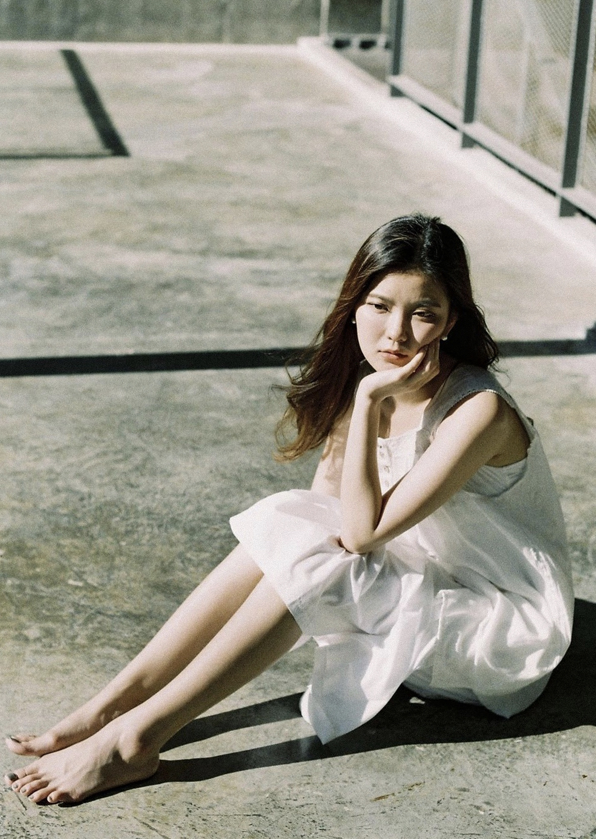 一个穿着白色连衣裙的年轻女子坐在混凝土地板上
