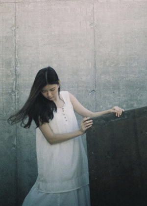 一个穿白裙子的年轻女子站在一块混凝土墙上