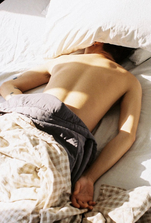 一个没有穿衬衫的年轻人正在一张带有白色床单和枕头的床上睡觉。