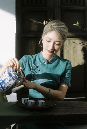 一位年轻女子坐在桌子旁 手里拿着一束蓝色和白色的花瓶和一杯茶。