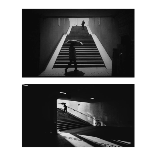 一张黑白照片 一个人带着伞走楼梯。