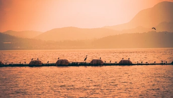 日落时分的广阔水面 人们在一艘船上 飞鸟在水面和远处的山脉上飞翔。