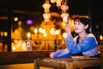 一位年轻女子坐在夜晚点着灯笼的桌子旁